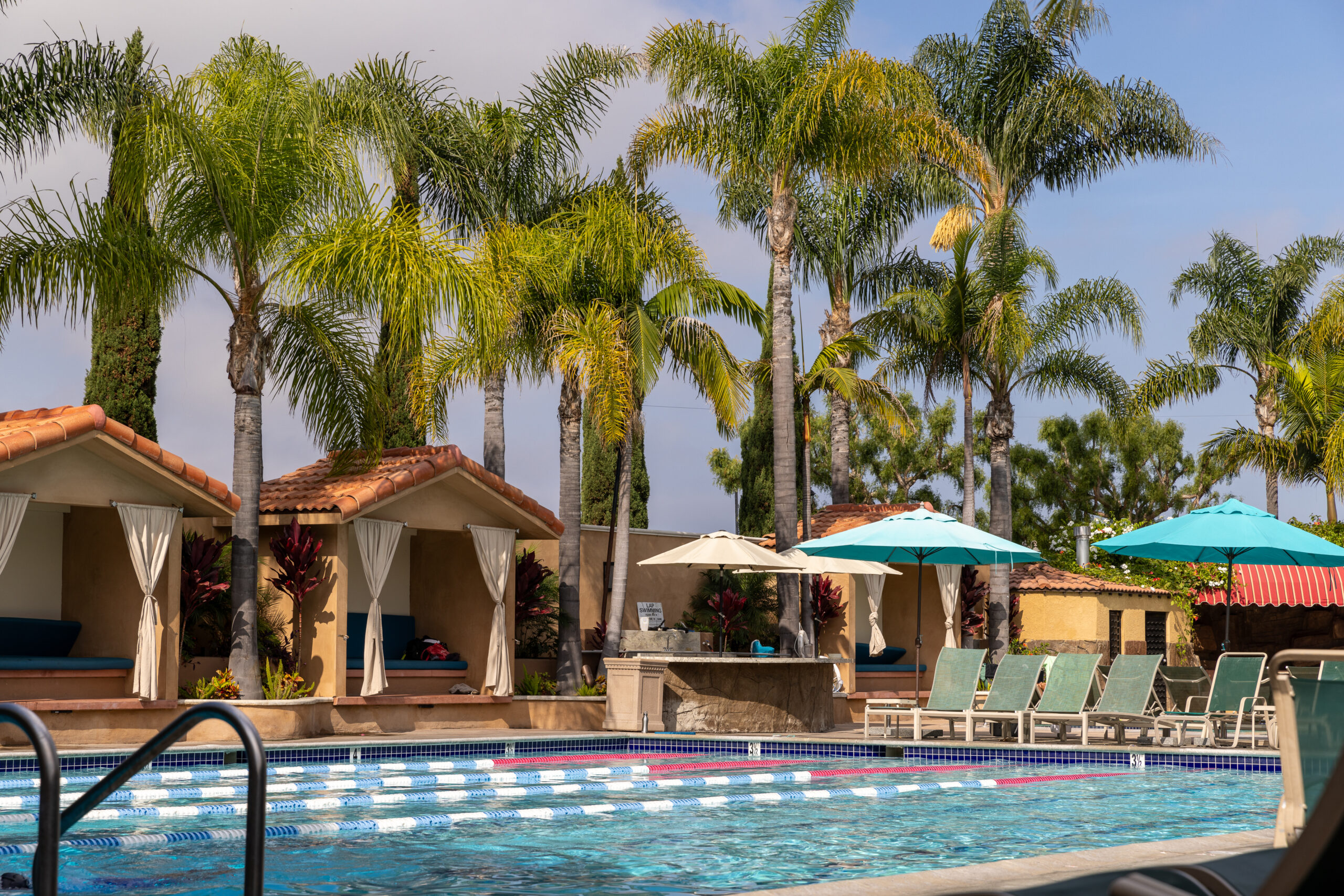 Lap pool with lounge chairs, umbrellas, and Mediterranean-style poolside buildings