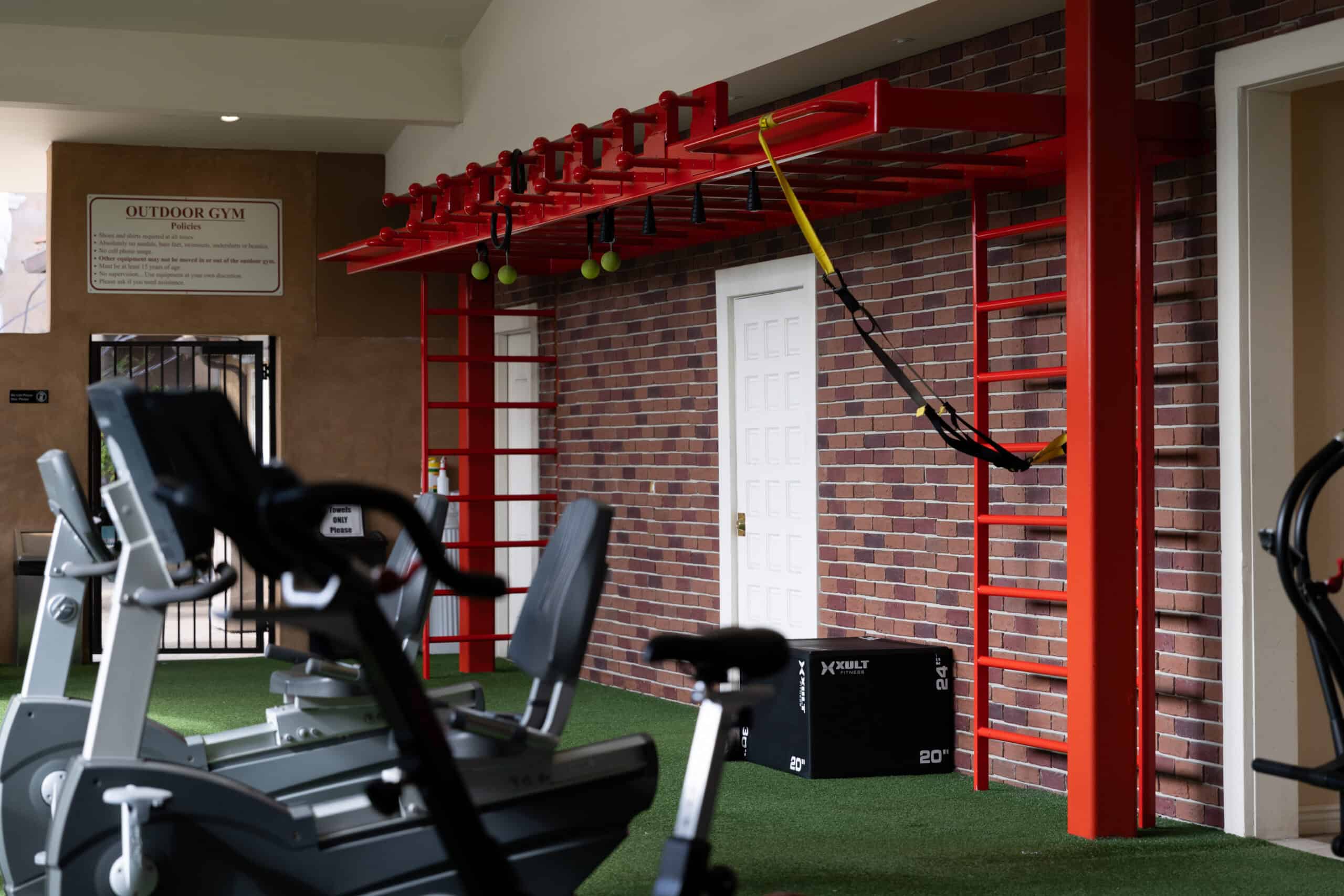 Outdoor gym — red functional training rig, turf floor, and equipment