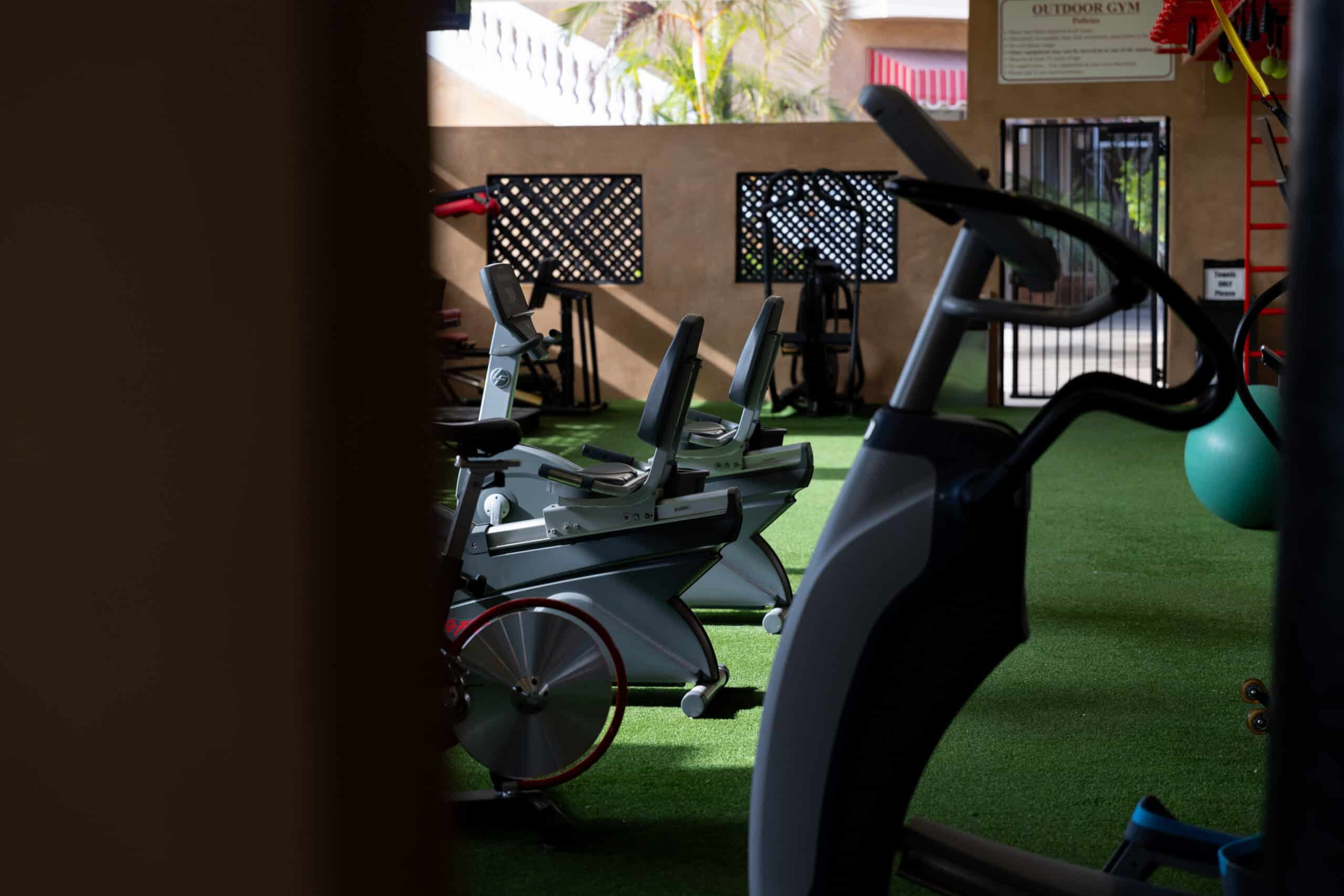 Outdoor gym — turf floor, cardio equipment, and policies sign